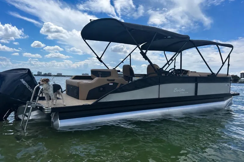 The Image of 2022 Barletta E24UC pontoon boat on water with a dog onboard, under a blue sky. - 0