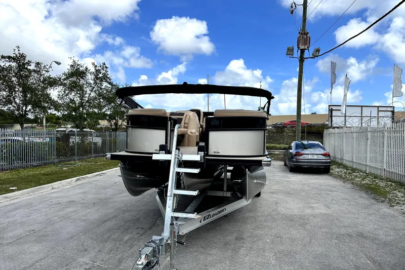 Slide: The Image of 2022 Barletta E24UC pontoon boat on trailer, parked outdoors under blue sky. - 2