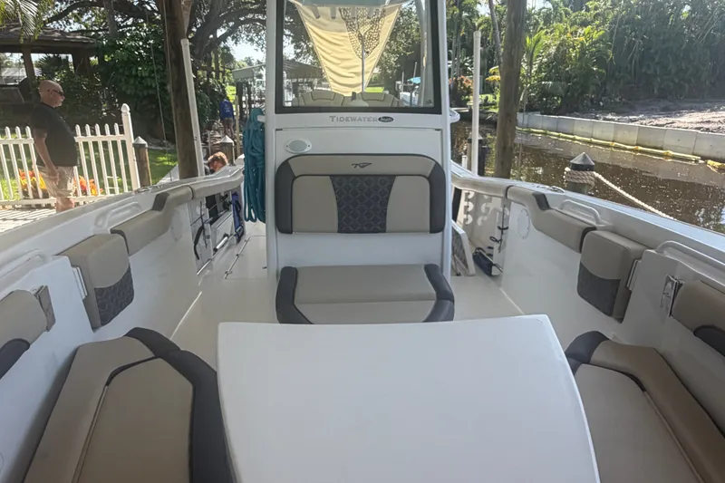 Slide: The Image of 2021 Tidewater 272 CC Adventure boat interior with seating and table, docked near lush greenery. - 30