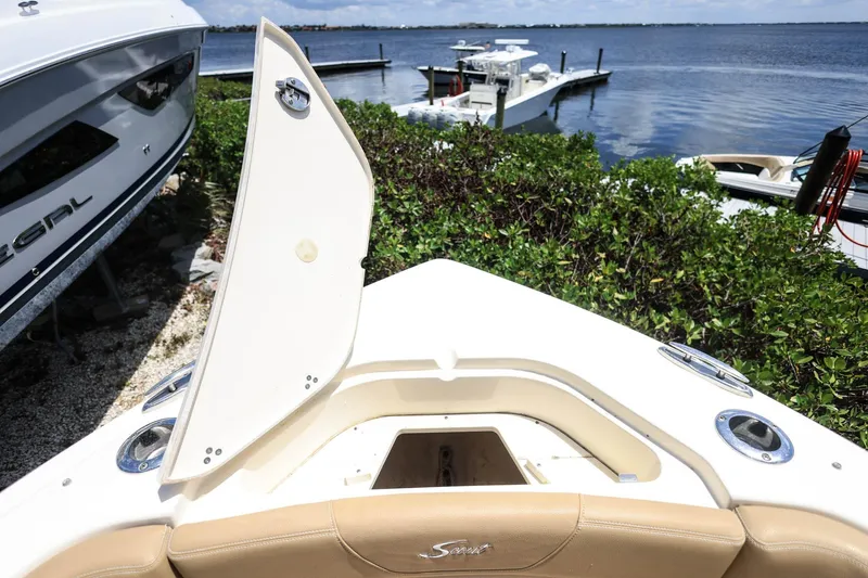 Slide: The Image of 2020 Scout 235 Dorado boat with open storage compartment, docked near lush greenery. - 28