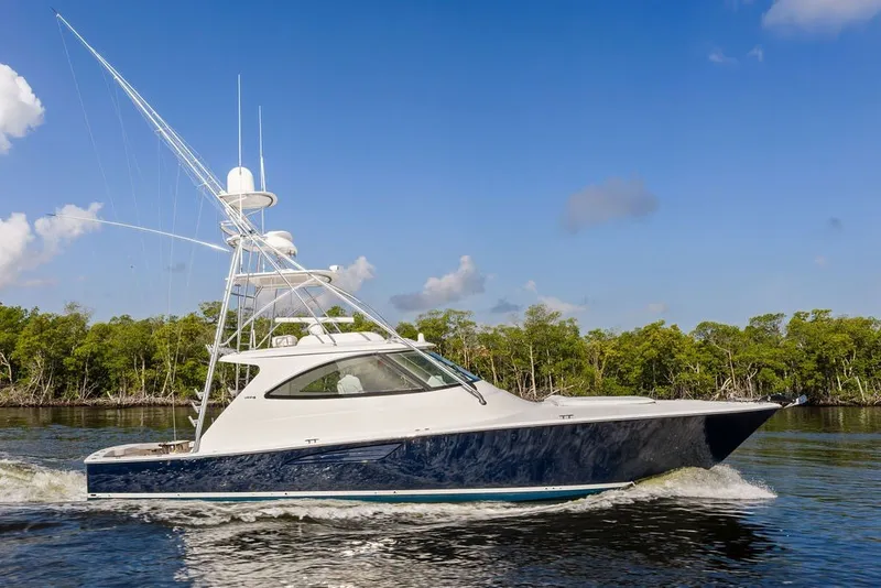Slide: The Image of 2021 Viking 52 Sport Tower yacht cruising on a sunny day, surrounded by lush greenery. - 0