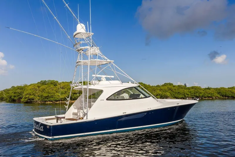 Slide: The Image of 2021 Viking 52 Sport Tower yacht cruising on calm waters near lush greenery. - 16