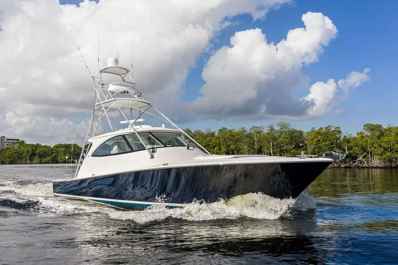 Slide: The Image of 2021 Viking 52 Sport Tower cruising on a sunny day with lush greenery in the background. - 1