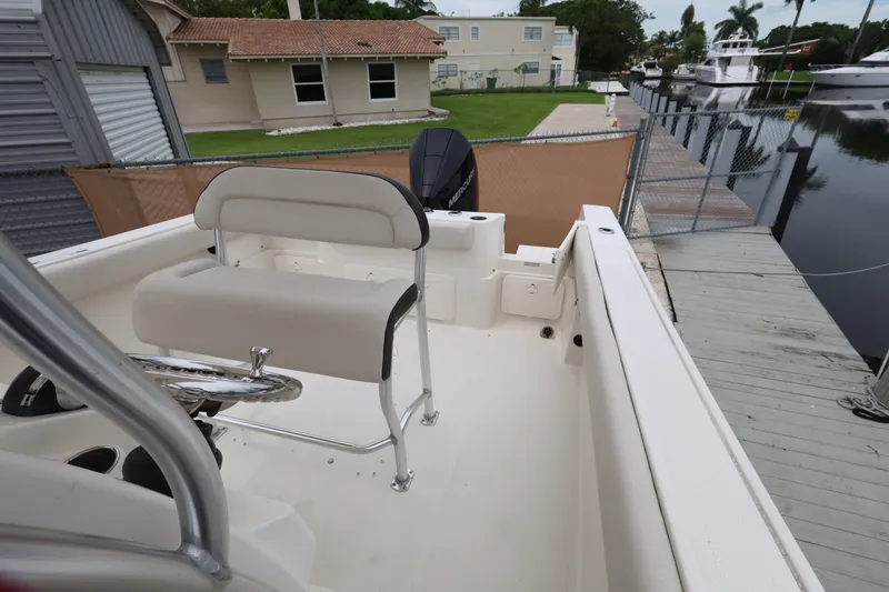 Slide: The Image of 2022 Sailfish 242 CC boat interior with seating and steering wheel, docked by a canal. - 17