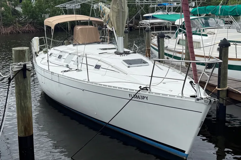 The Image of A white sailboat docked, featuring a beige sunshade, surrounded by other boats. - 0