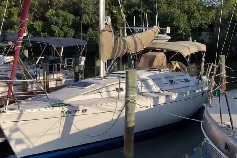 The Image of 1990 Beneteau First 35s5 sailboat docked, featuring beige covers and lush greenery background. - 1
