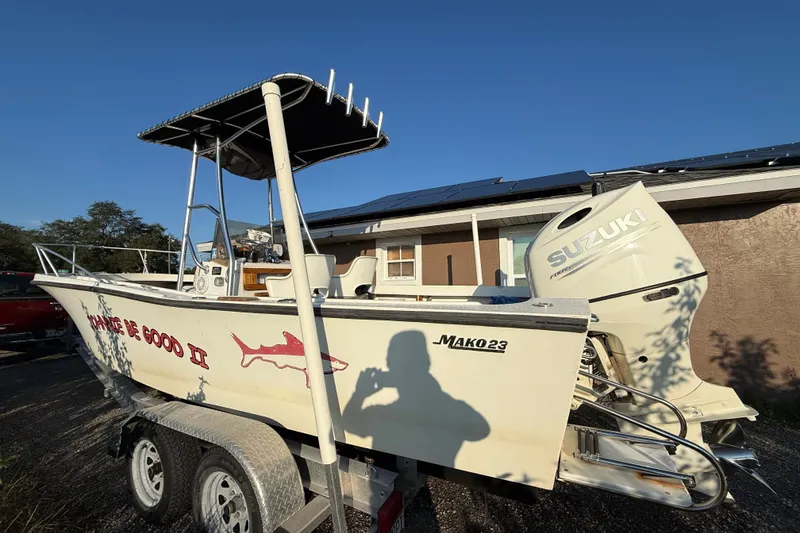 Slide: The Image of 1977 Mako 235 boat with Suzuki engine on trailer, parked near a house. - 2
