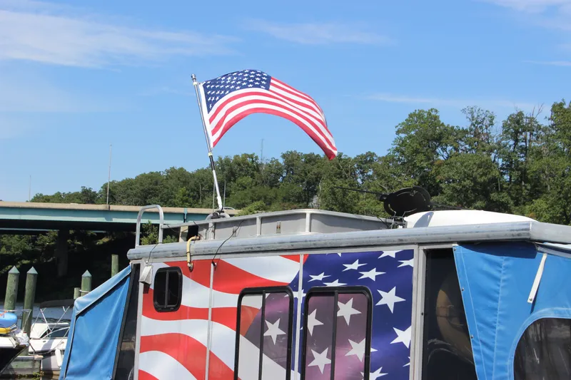 Slide: The Image of 1994 Sun Tracker Party Cruiser 32 with American flag, docked near trees and bridge. - 26