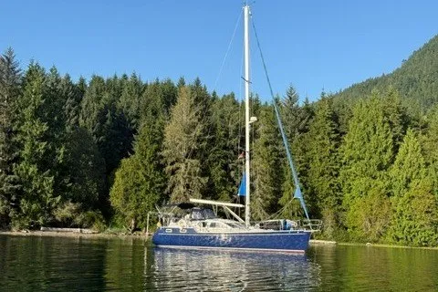 The Image of Sailboat Nauticat 37 (2002) on tranquil water, surrounded by lush green forest. - 0