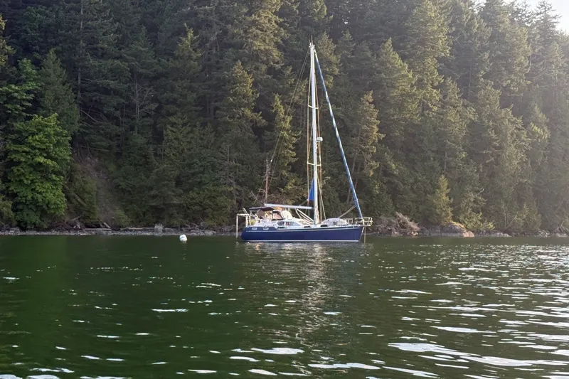 Slide: The Image of Sailboat Nauticat 37 (2002) anchored near lush forested shoreline. - 2