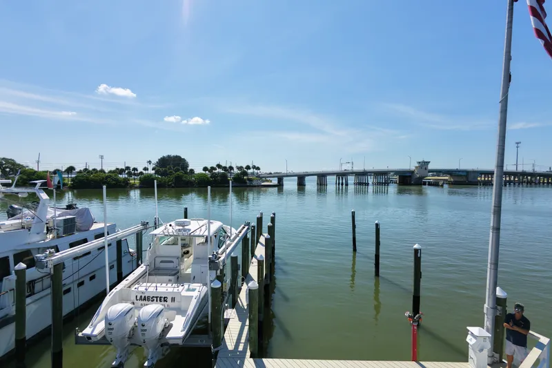 Slide: The Image of 2023 Pursuit DC 326 boat docked by a scenic waterfront with a bridge in the background. - 26