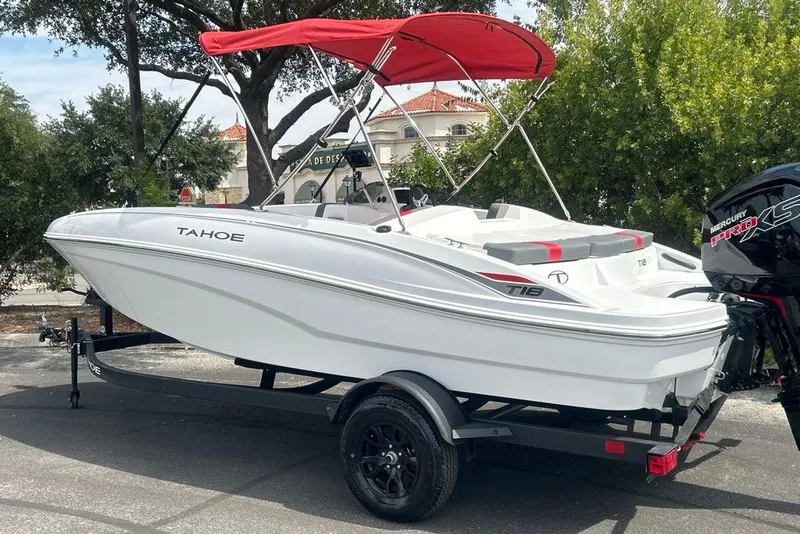 Slide: The Image of 2027 Tahoe T18 boat with red canopy on trailer, parked outdoors. - 2