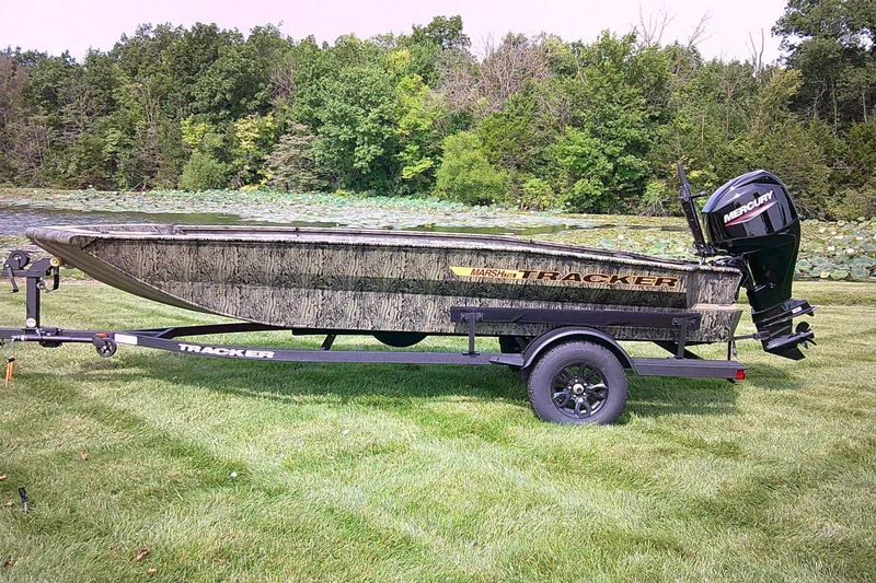 The Image of 2027 Tracker Grizzly 1756 T Marsh boat on trailer, parked on grass near a lake. - 0