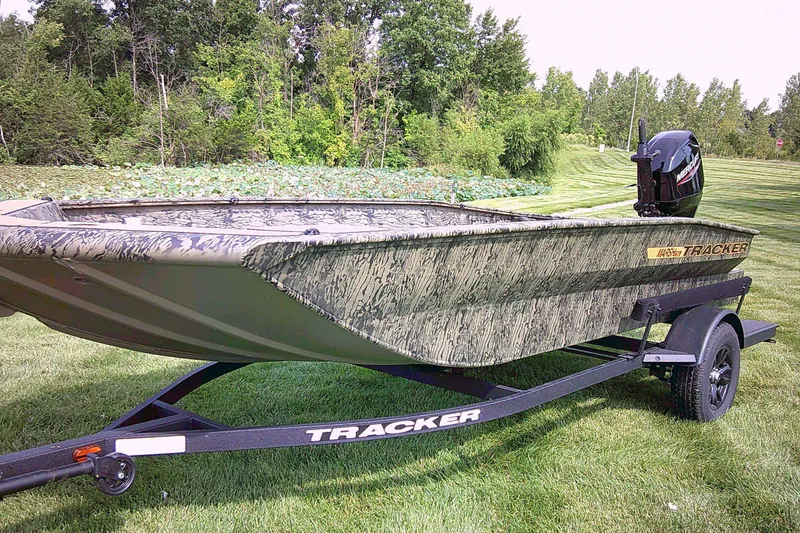 The Image of 2027 Tracker Grizzly 1756 T Marsh boat on trailer, camo design, parked on grass. - 0