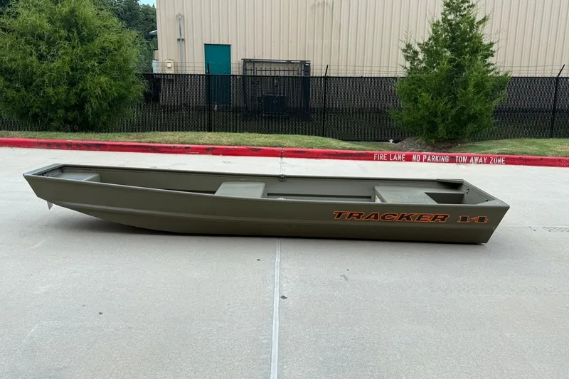 The Image of 2027 Tracker Grizzly 14 Jon boat on concrete surface, near a building and greenery. - 0