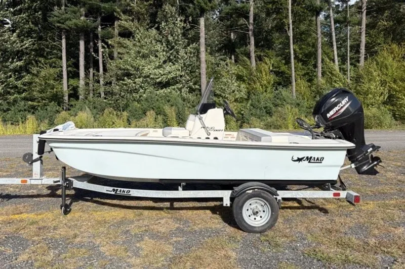 Slide: The Image of 2026 Mako Pro Skiff 13 CC boat on trailer, parked outdoors near trees. - 2