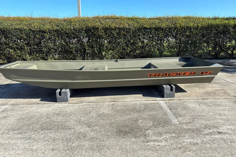The Image of 2027 Tracker Grizzly 15 Jon boat on concrete blocks, outdoors with hedge background. - 0