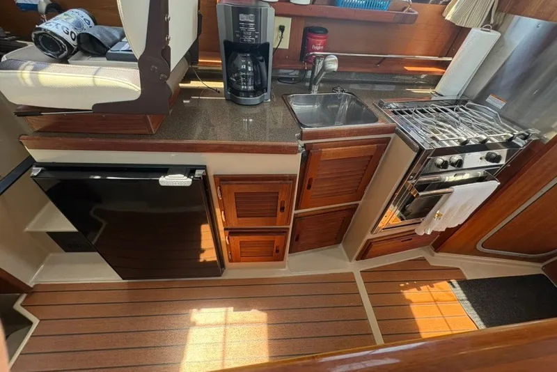 Slide: The Image of 2017 Ranger Tugs R-27 galley with stove, sink, fridge, and wooden cabinetry. - 49