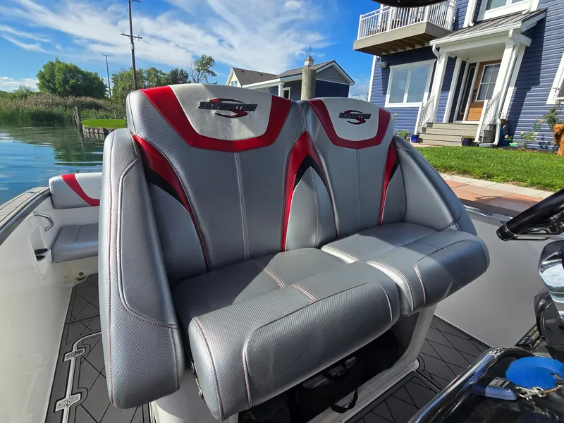 Slide: The Image of The 2017 Sunsation 32 CCX seats are gray with red accents, set against a waterfront house. - 8