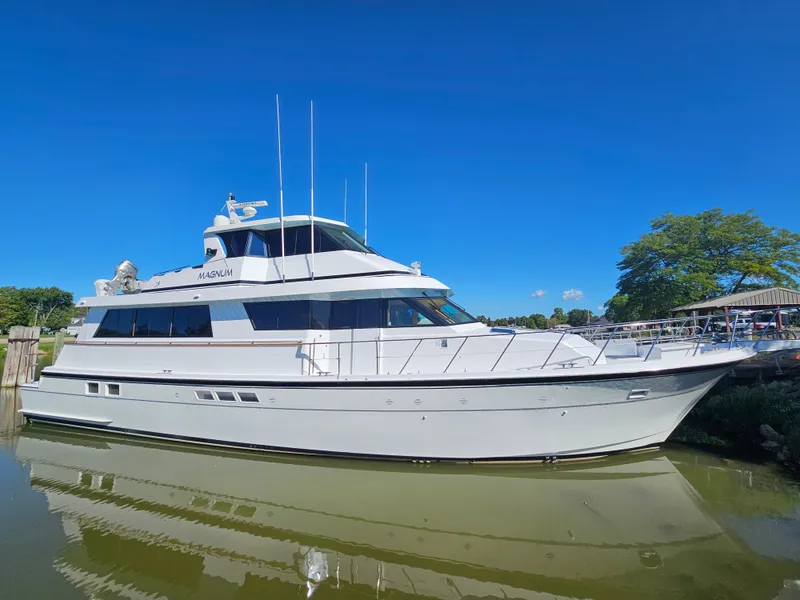 The Image of A white 1991 Hatteras 70 Cockpit Motor Yacht is docked in the water, surrounded by trees. - 0