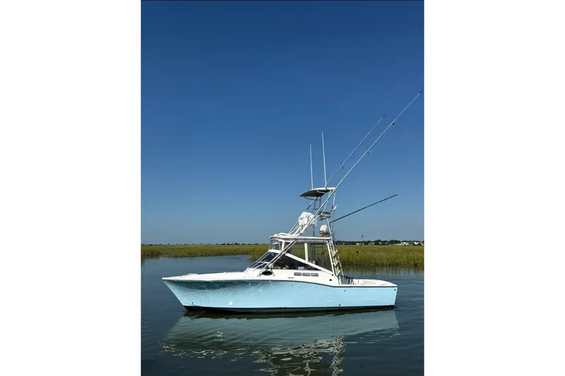 The Image of 1996 Carolina Classic 28 boat on calm water under clear blue sky. - 0