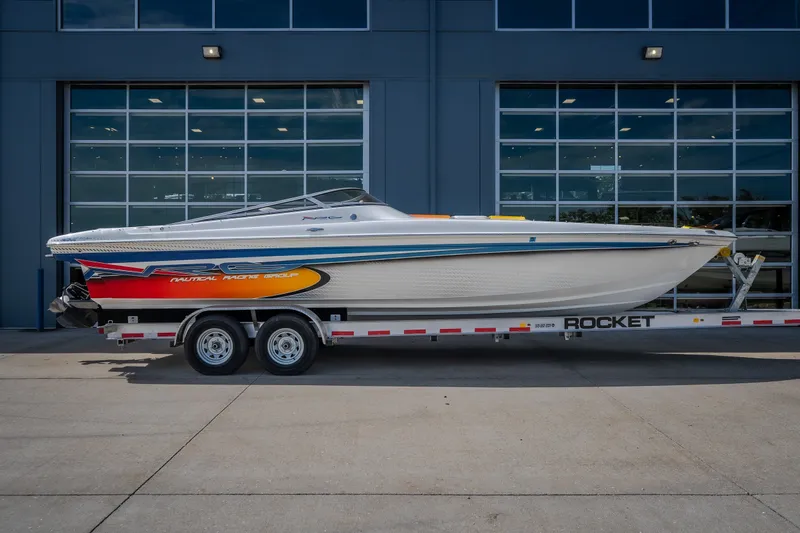 Slide: The Image of 2012 Nautical NRG 30 boat on trailer, vibrant design, parked outside a modern building. - 50