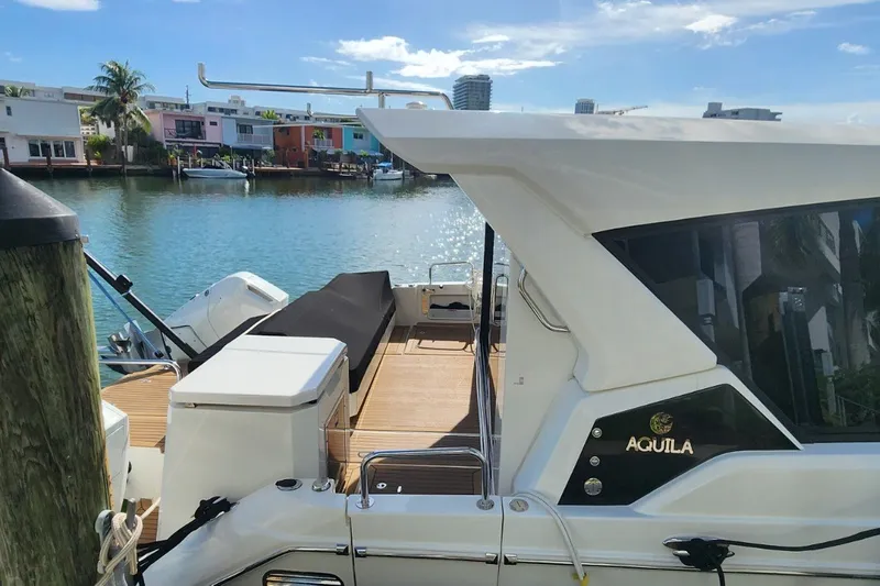 Slide: The Image of 2024 Aquila 36 Sport yacht docked by waterfront homes under a clear blue sky. - 21