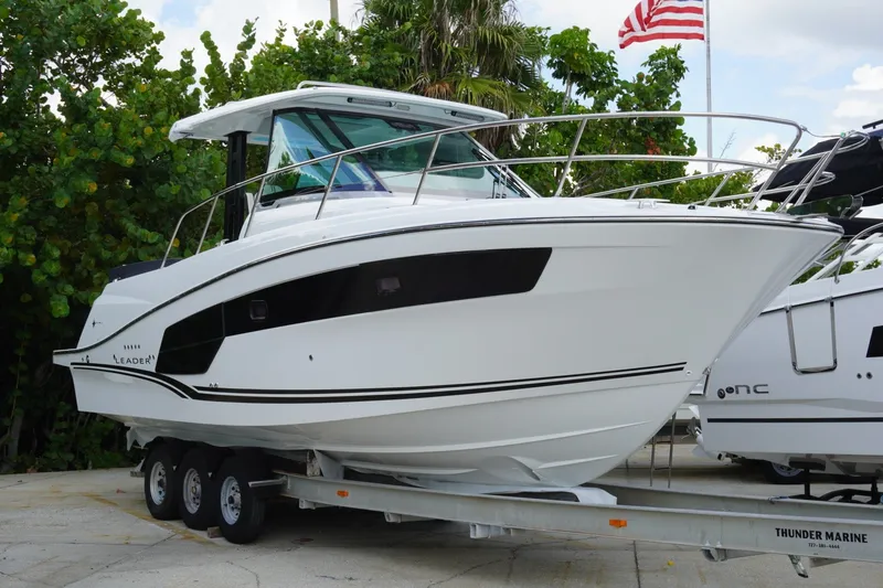 The Image of 2027 Jeanneau Leader 10.5 WA Series 2 boat on trailer, surrounded by greenery and American flag. - 0