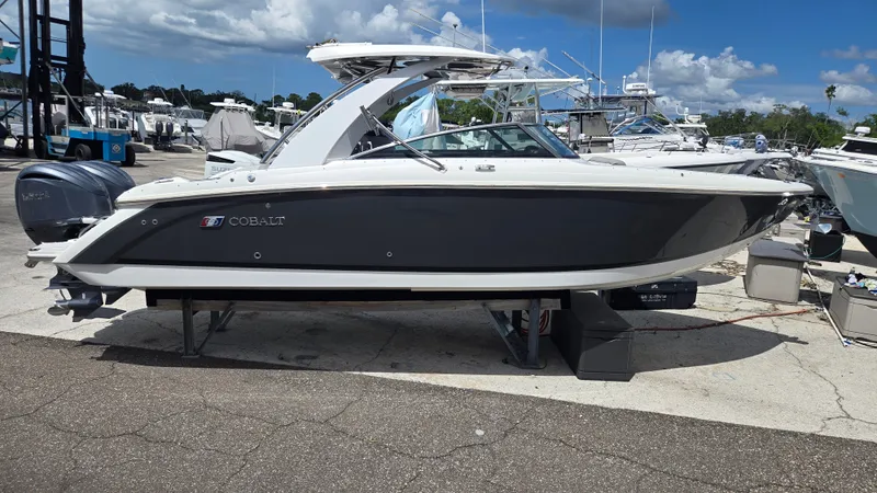 The Image of A sleek 2023 Cobalt 30SC boat is on a trailer in a marina. - 0