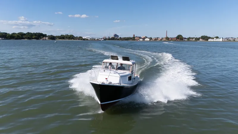 Slide: The Image of A 1959 Dyer 29 Trunk Cabin boat cruising on calm waters with a cityscape in the background. - 3