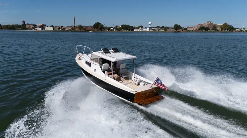 The Image of A 1959 Dyer 29 Trunk Cabin boat speeds across the water, with a cityscape in the background. - 0