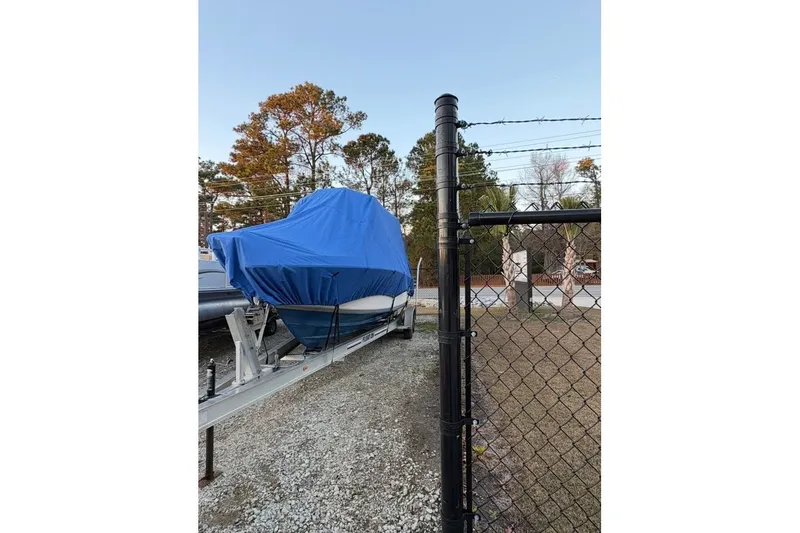 Slide: The Image of 2003 Contender 23 Open boat covered in blue tarp on trailer, near chain-link fence. - 3