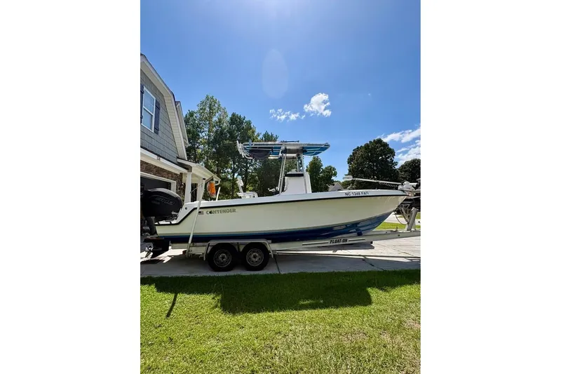 Slide: The Image of 2003 Contender 23 Open boat on trailer, parked beside a house under a clear blue sky. - 2