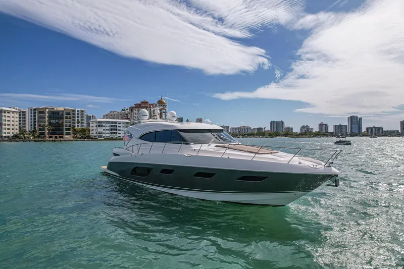 Slide: The Image of 2015 Riviera 6000 Sport Yacht cruising in sunny coastal waters with city skyline backdrop. - 5