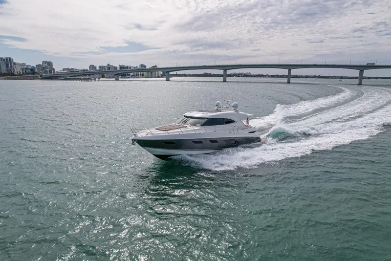 Slide: The Image of 2015 Riviera 6000 Sport Yacht cruising on open water near a bridge. - 16