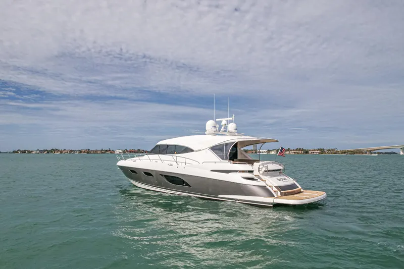 The Image of 2015 Riviera 6000 Sport Yacht cruising on open water under a cloudy sky. - 1
