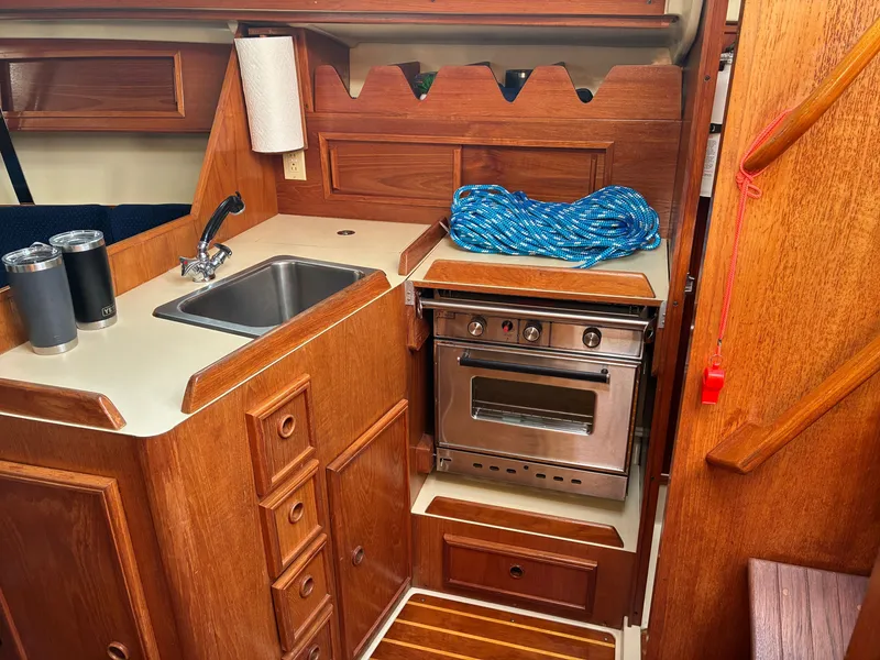 Slide: The Image of The galley of a 1988 Pearson 33-2 with a sink, stove, and wooden cabinetry. - 27