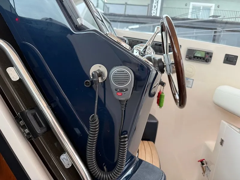 Slide: The Image of The image shows the helm of a 2013 Tiara Yachts 3600 Open with a microphone and wooden steering wheel. - 17