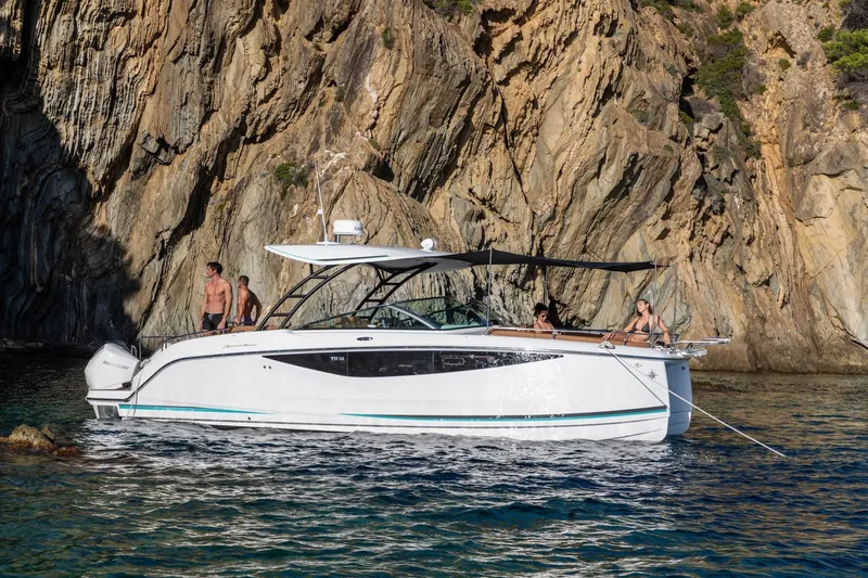 Slide: The Image of 2027 Jeanneau TH33 boat anchored near rocky cliffs with people on board. - 6