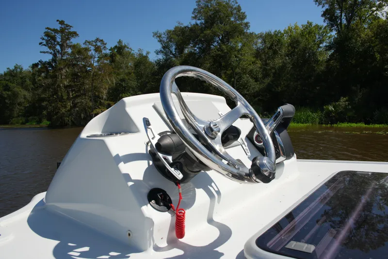 Slide: The Image of 2024 Costa Custom Boats 264HC steering wheel on a sunny day, surrounded by lush greenery. - 53