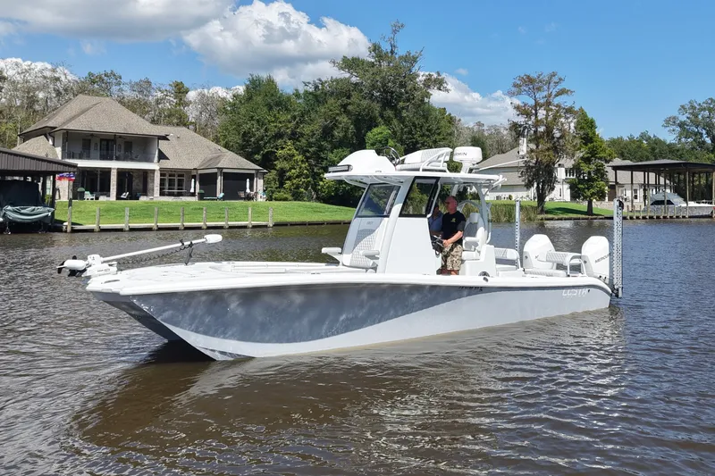 Slide: The Image of 2024 Costa Custom Boats 264HC on a scenic river with houses in the background. - 16