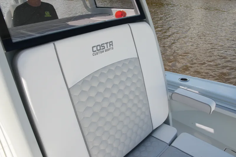Slide: The Image of 2024 Costa Custom Boats 264HC interior seating with logo, on water. - 55