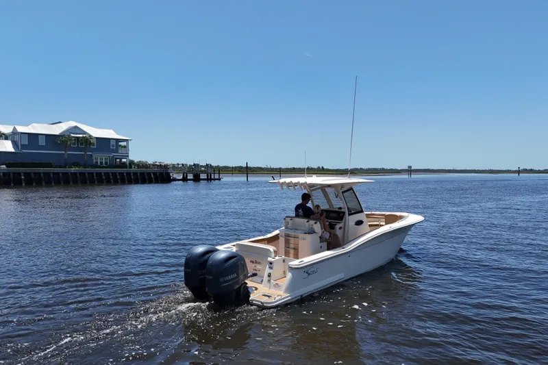 Slide: The Image of 2021 Scout 277 LXF boat cruising on a sunny day near waterfront homes. - 16