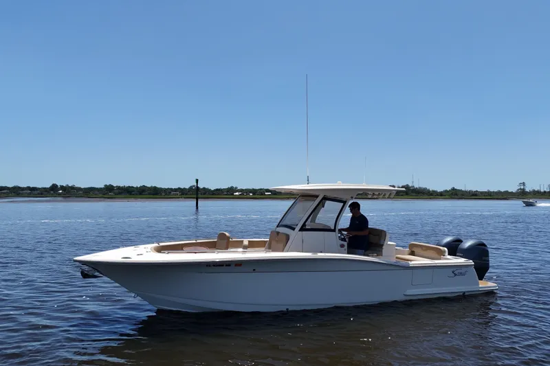 Slide: The Image of 2021 Scout 277 LXF boat cruising on a calm river under clear blue skies. - 22