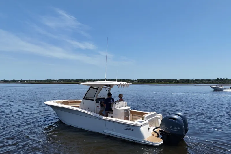 Slide: The Image of 2021 Scout 277 LXF boat cruising on a calm lake under a clear blue sky. - 23
