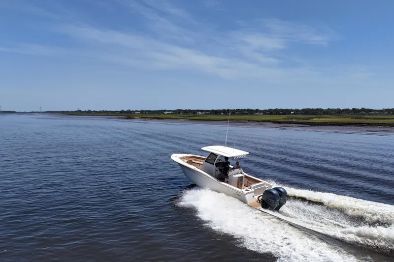 Slide: The Image of 2021 Scout 277 LXF boat cruising on a calm river under a clear blue sky. - 8