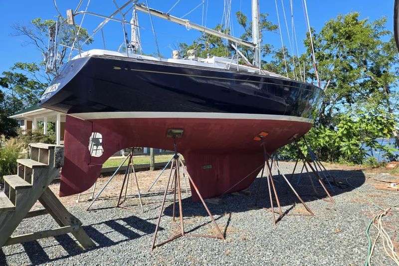 The Image of 1978 Bristol 35.5 sailboat on stands, displayed outdoors on gravel with trees in background. - 0