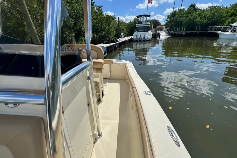 Slide: The Image of 2022 Scout 215 XSF boat docked on a sunny day, surrounded by lush greenery. - 26