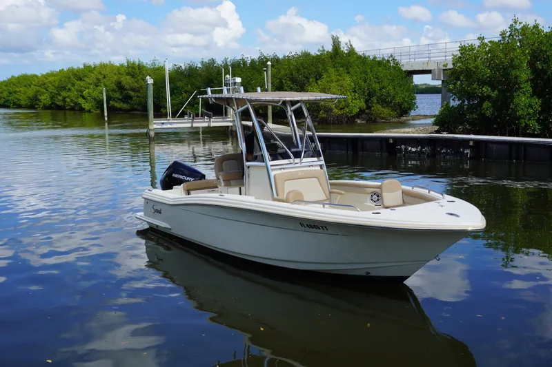 Slide: The Image of 2022 Scout 215 XSF boat on calm water near lush greenery and a bridge. - 8