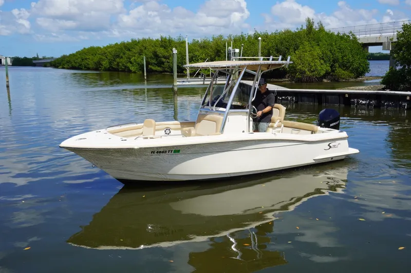 Slide: The Image of 2022 Scout 215 XSF boat on calm water with lush greenery background. - 2